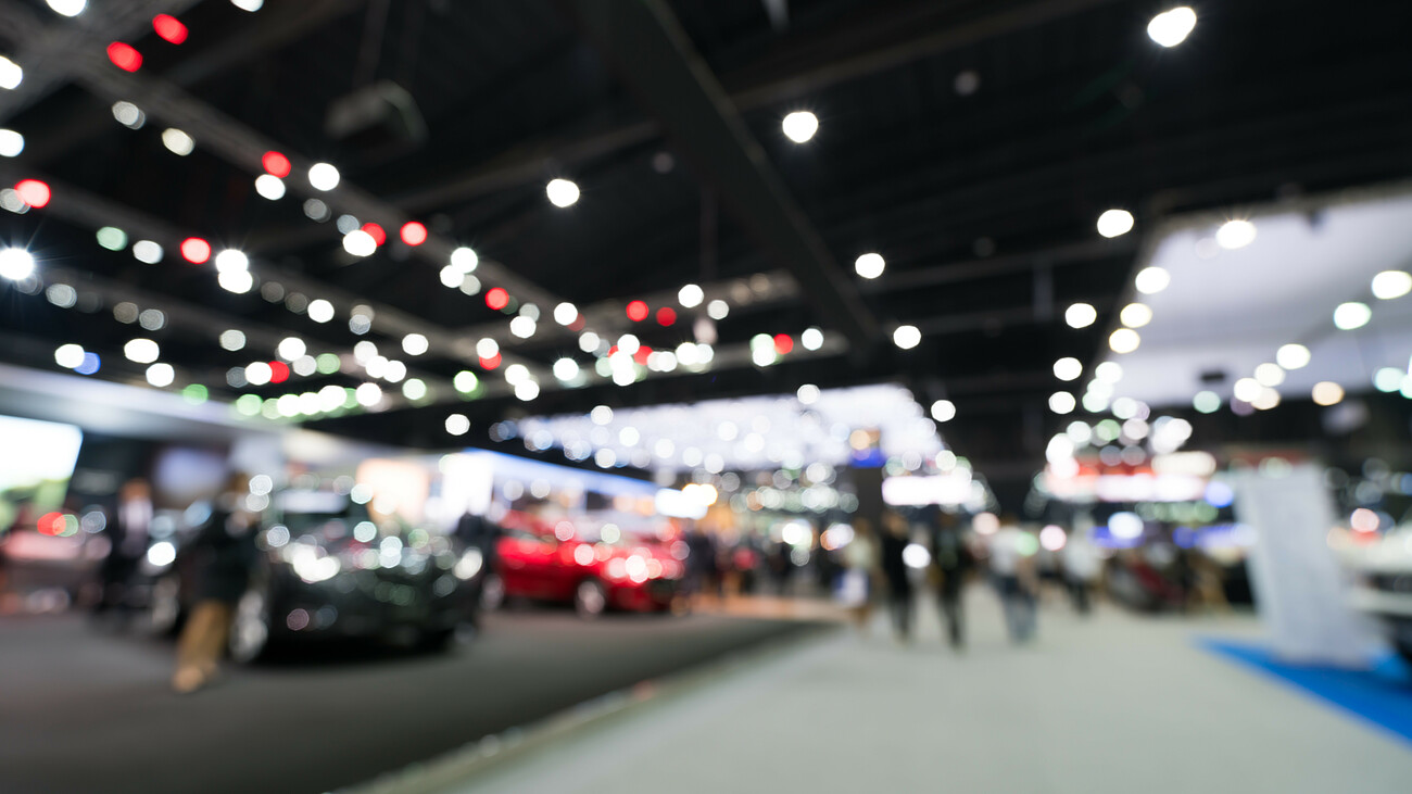 Blurred, defocused background of public event exhibition hall showing cars and automobiles, business commercial event concept