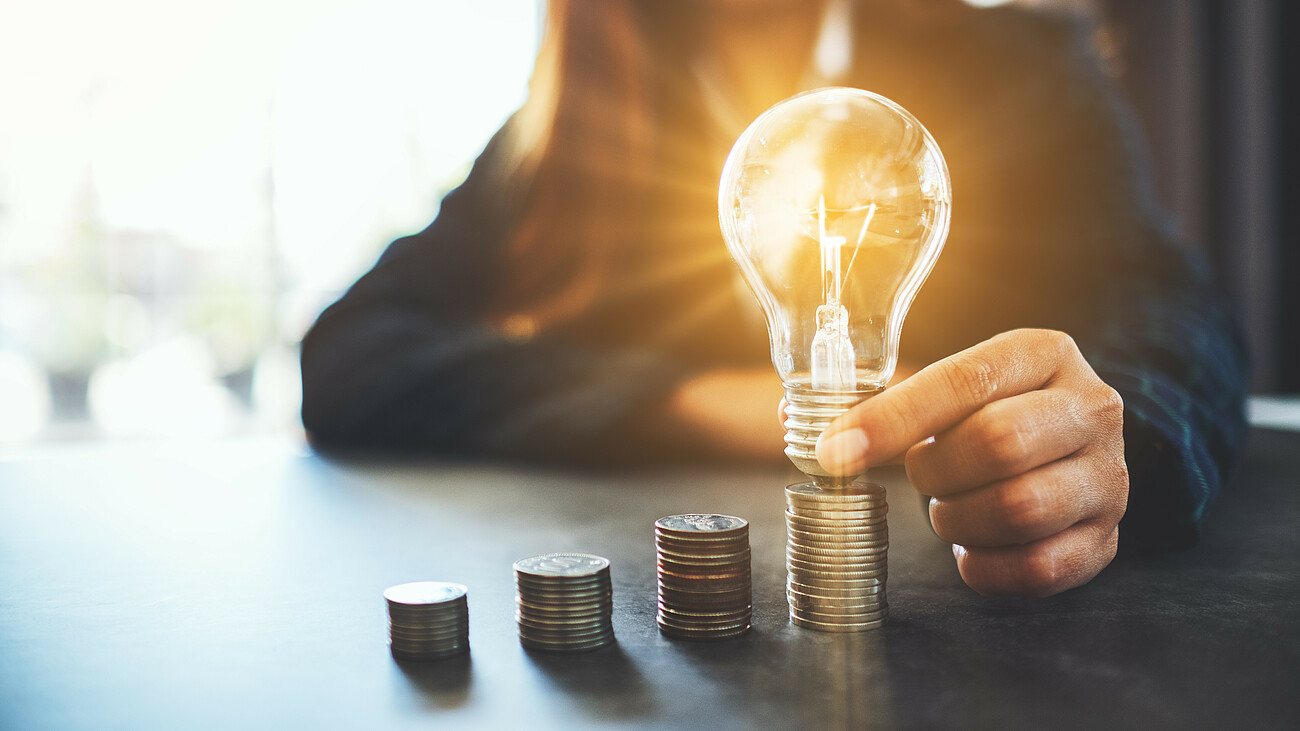Businesswoman holding and putting lightbulb on coins stack on table for saving energy and money concept